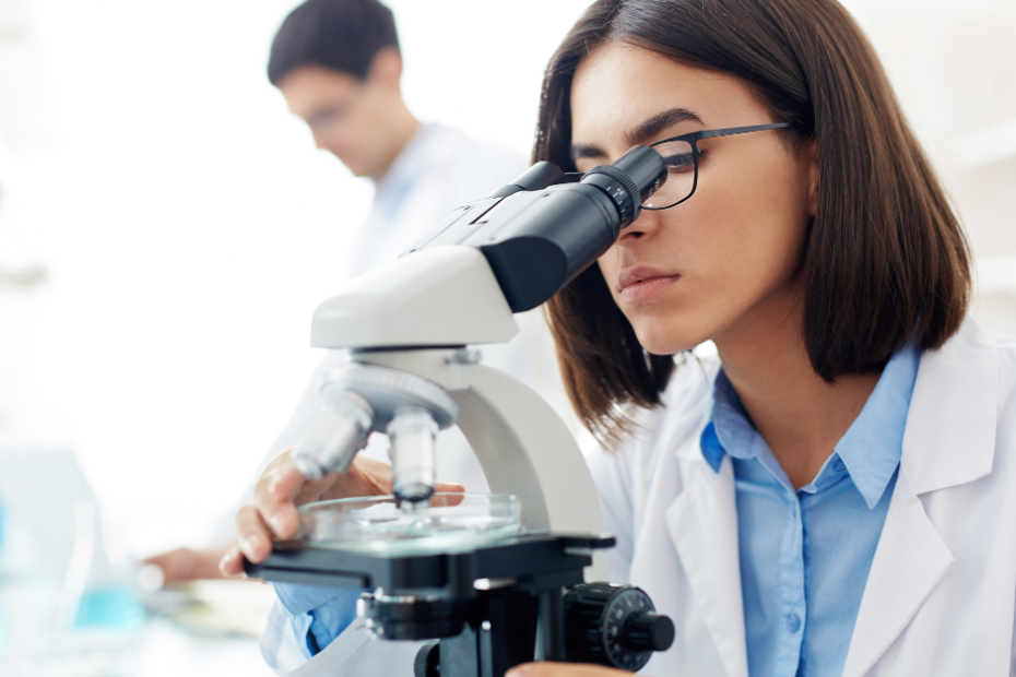 Chica viendo con el microscopio lo que hay en el recipiente de cristal