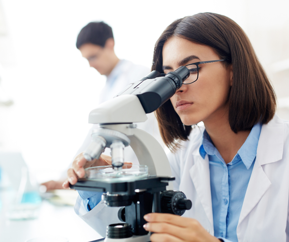 Chica viendo con el microscopio lo que hay en el recipiente de cristal