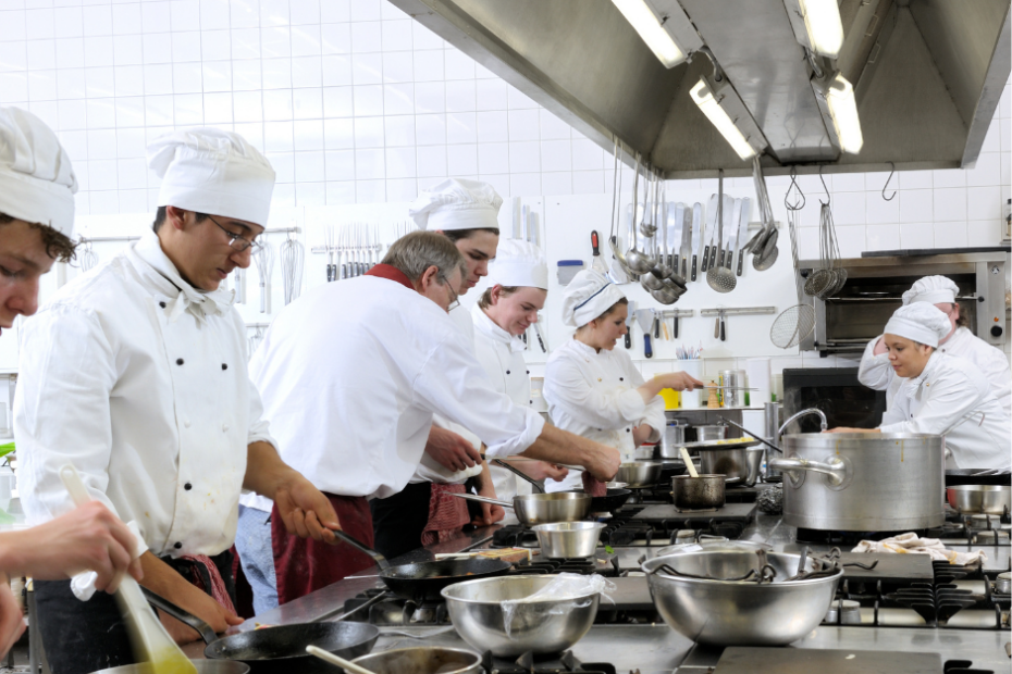 Grupo de cocineros cocinando mientras el chef enseña al cocinero aprendiz